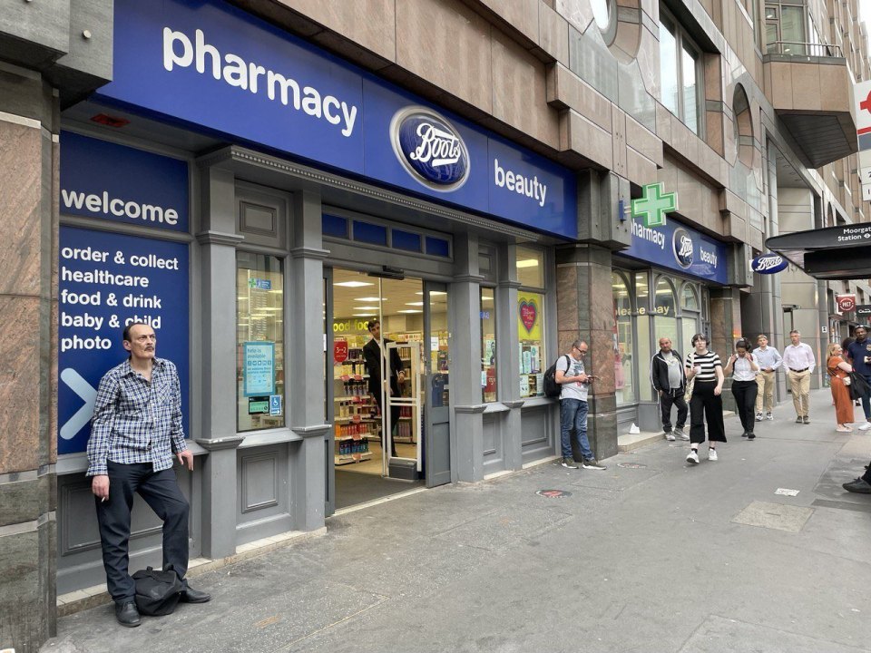 Витрина аптеки Boots с вывеской pharmacy на торговой улице, прохожие у входа