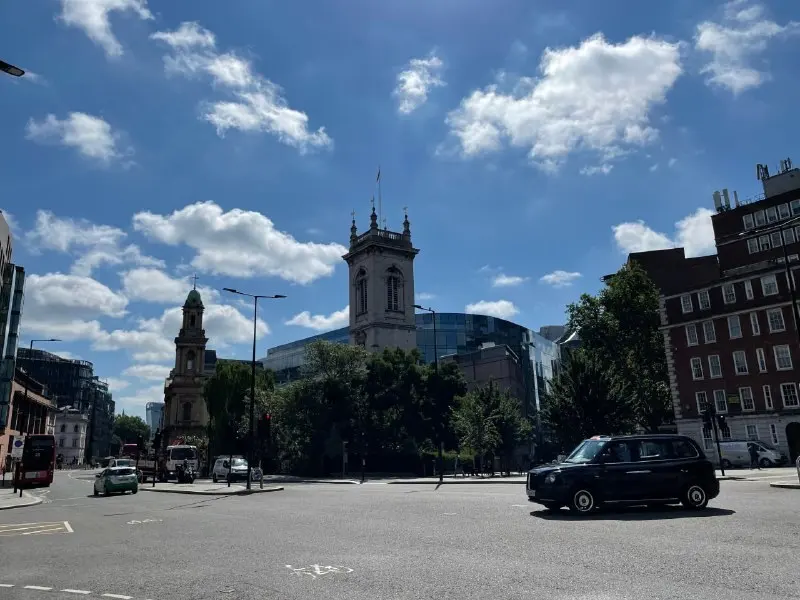 A City of London square with a church tower and a black cab