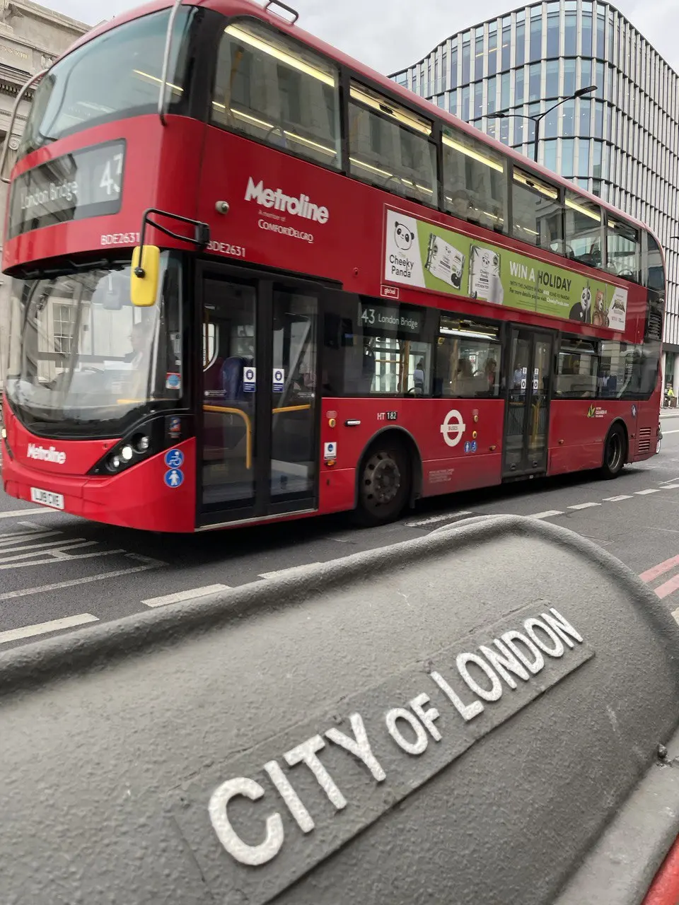 A red double-decker bus passing a stone City of London marker