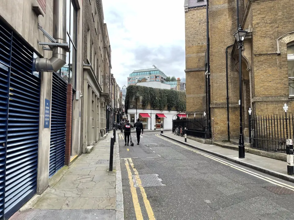 A narrow street in the City of London with brick buildings and a street lamp