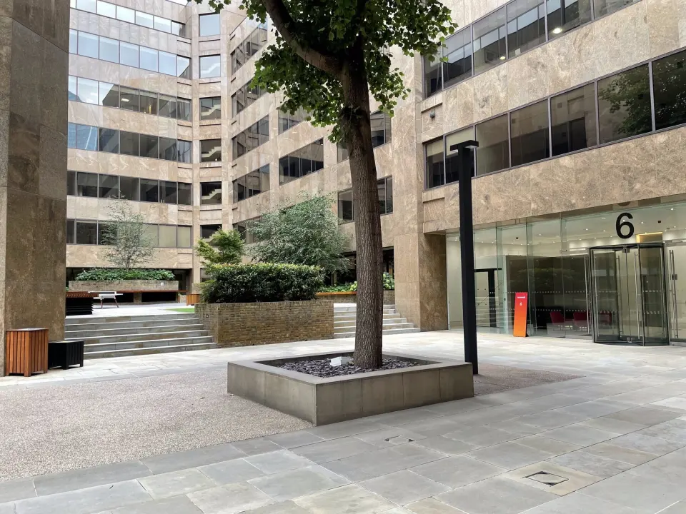 Courtyard of an office block in the City of London: stone facade, glass revolving doors, a tree in a concrete planter