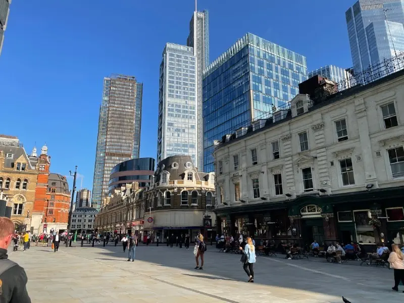 A City of London street with pedestrians on the pavement and office towers behind