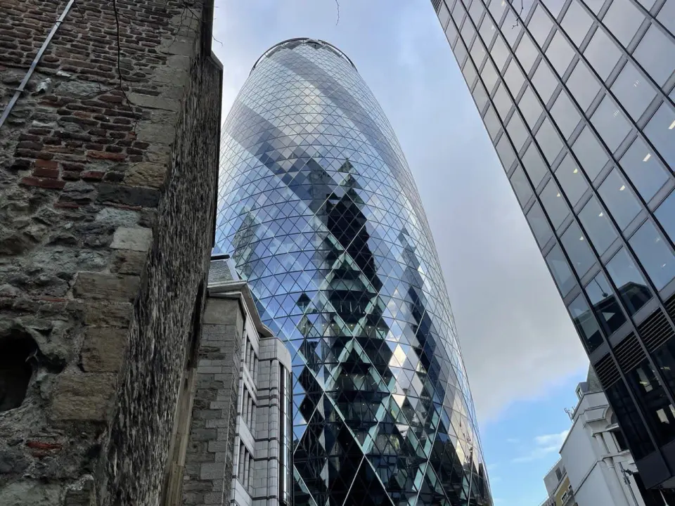 A glass tower in the City behind an old brick wall