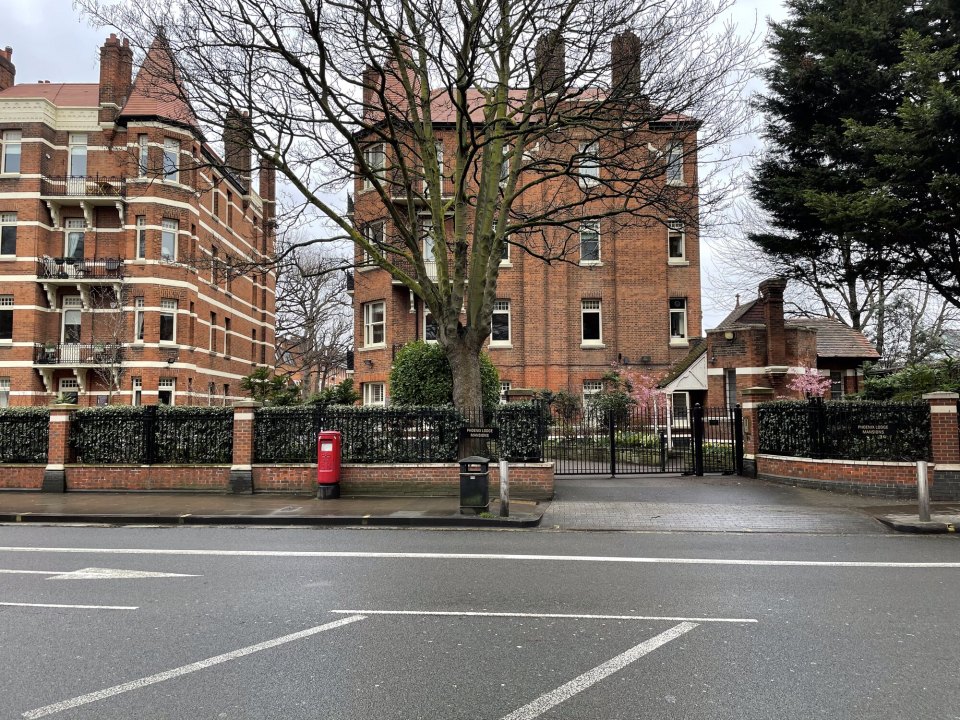 A Hammersmith street with red-brick residential blocks and a brick garden wall topped with a hedge and railings