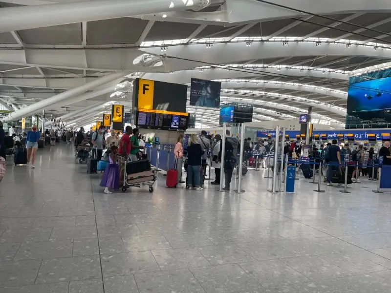 Passengers with suitcases and trolleys in a Heathrow airport terminal