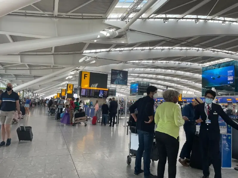 Passengers with trolleys and suitcases in a Heathrow airport terminal