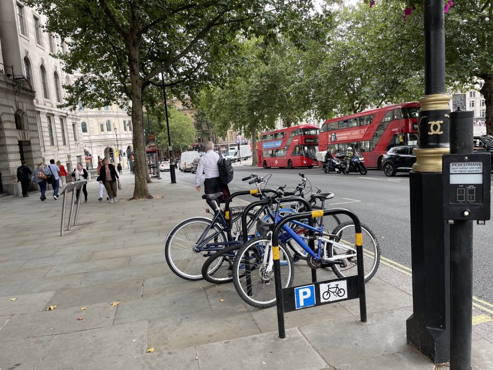 Cycle parking stands on a London street with red buses passing behind