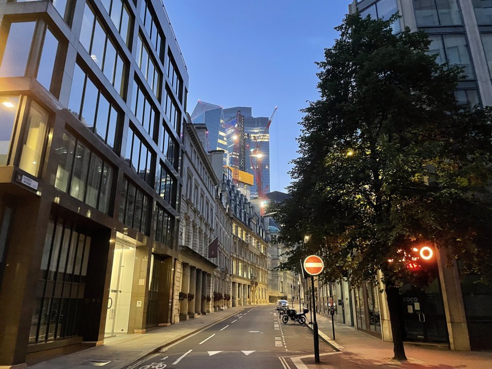 A City of London business street with modern offices and construction cranes at dusk