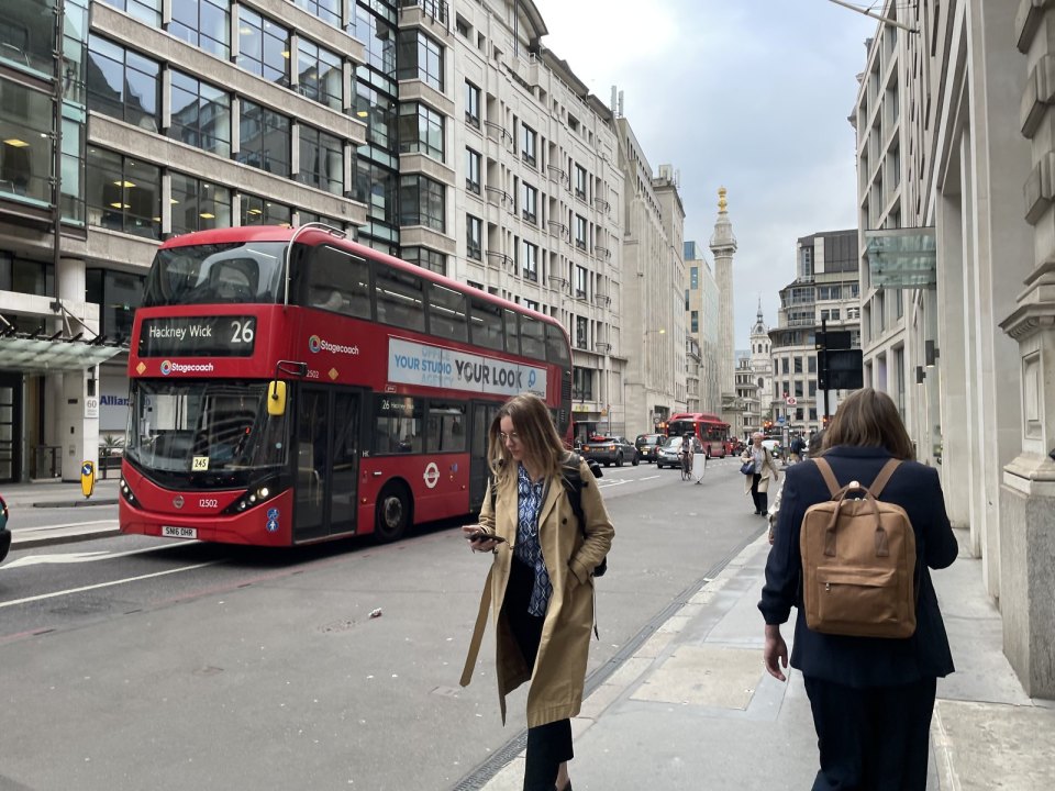 An everyday London street with a red bus and passers-by