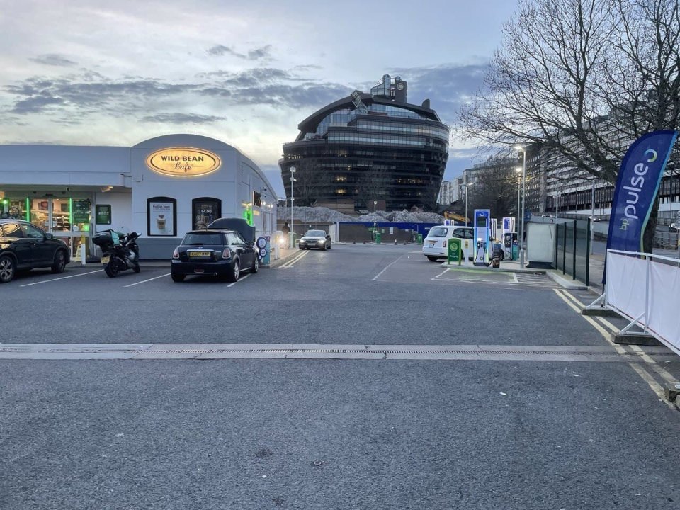 A petrol station forecourt in London with cars and City Hall in the distance