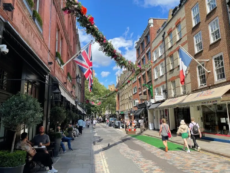 A London shopping street with shopfronts, flags strung above the road and passers-by carrying bags