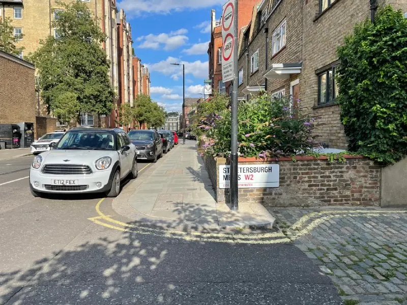 Narrow London street with cars parked along a yellow line and parking zone signs