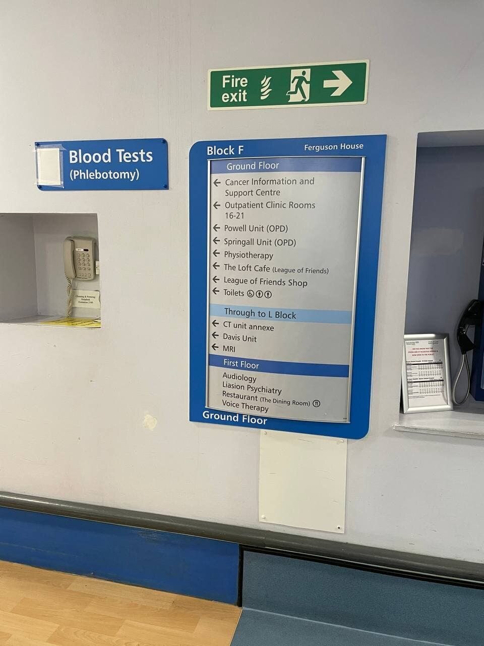 UK hospital corridor with a Blood Tests (Phlebotomy) sign and a department wayfinding board