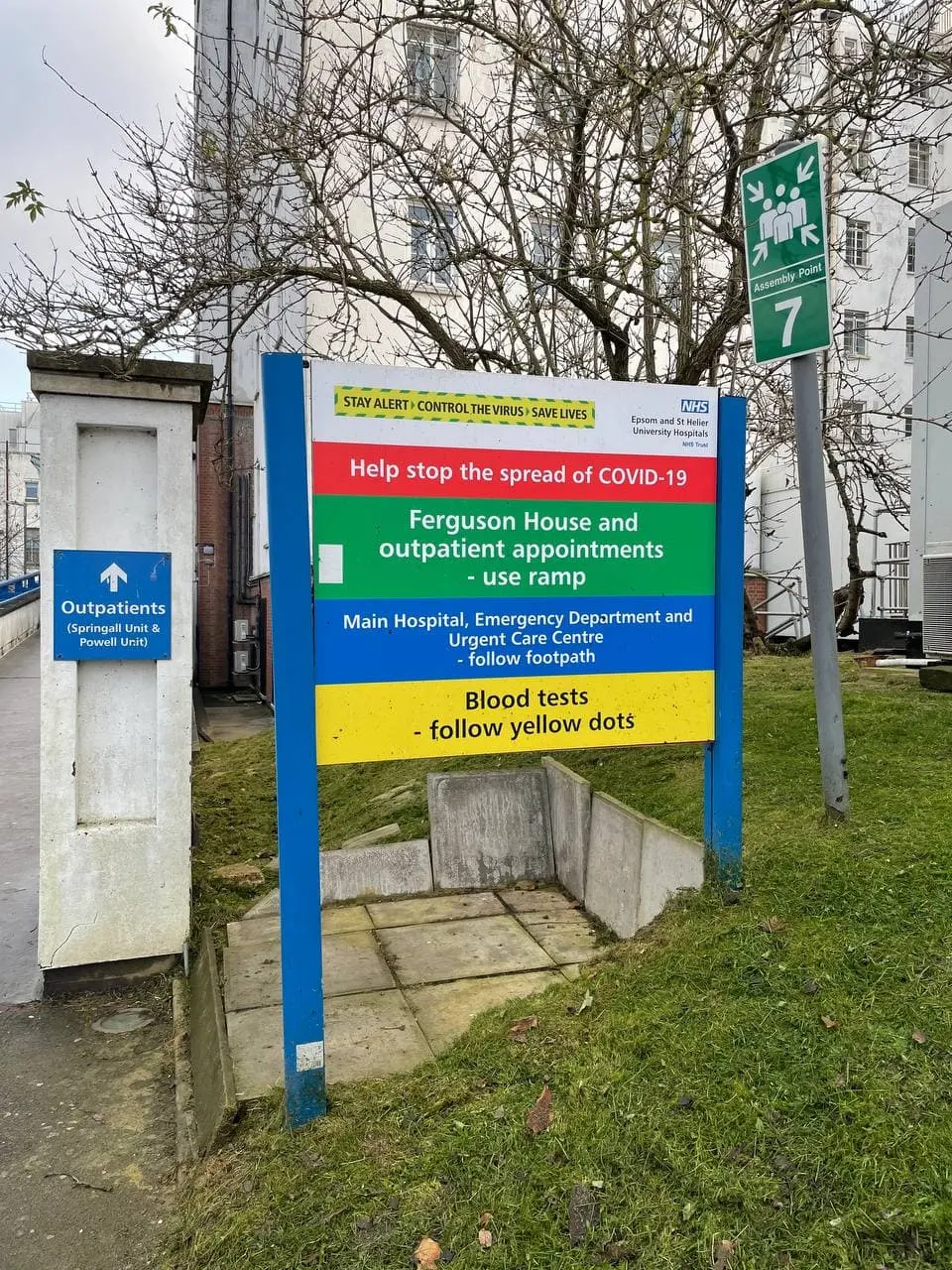 Blue NHS wayfinding sign at the entrance to a London hospital: outpatients, emergency department and blood tests