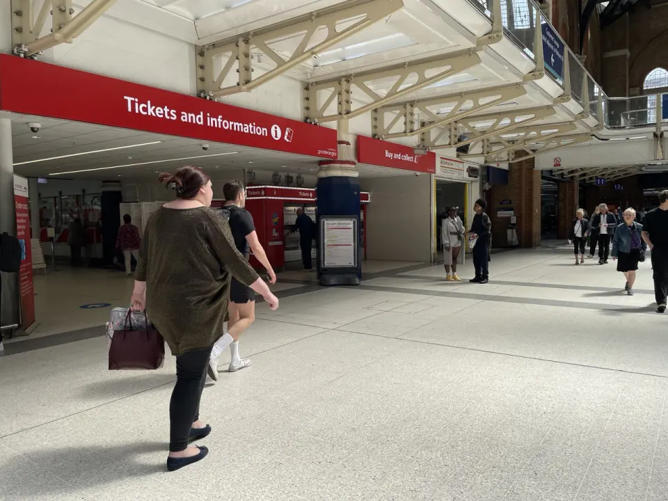 A passenger with bags walks through a London station hall past the ticket office
