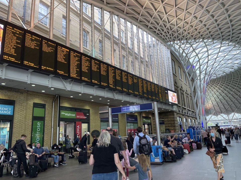 Табло отправления поездов на вокзале King's Cross в Лондоне, пассажиры ждут под стеклянной крышей