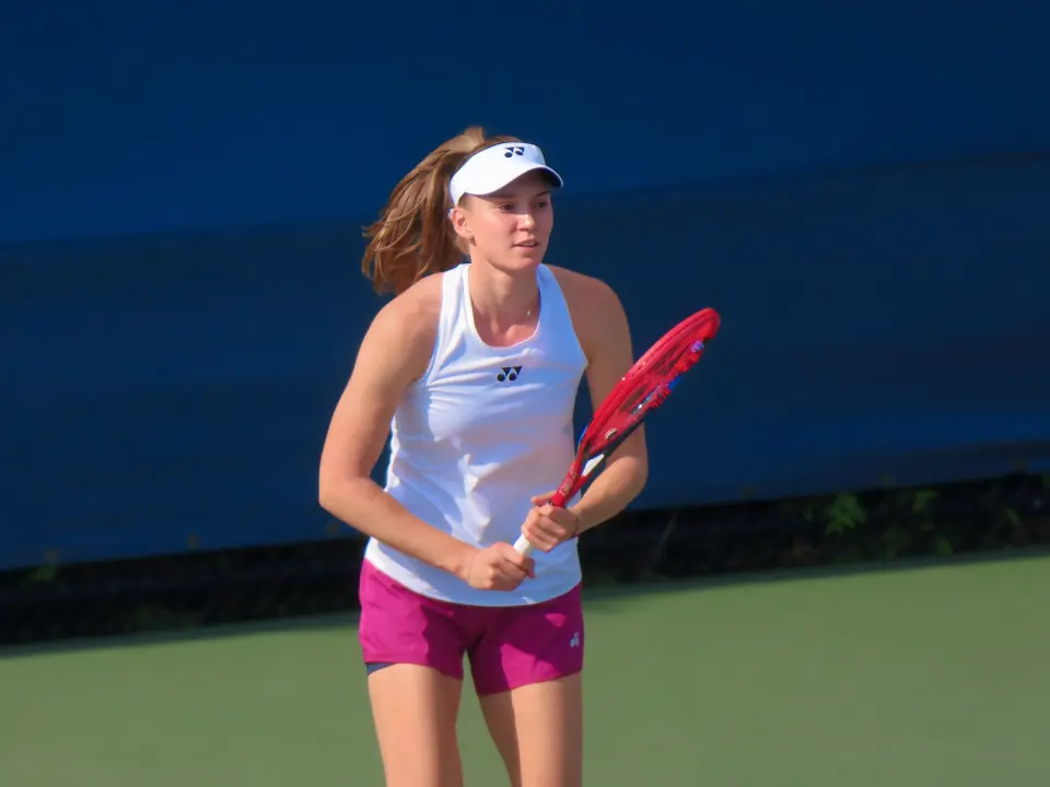 Елена Рыбакина на корте US Open с ракеткой в руках, в белой майке и розовых шортах