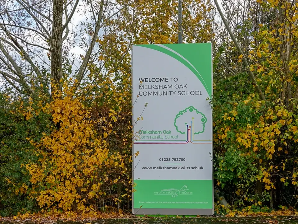 Указатель «Welcome to Melksham Oak Community School» у входа в английскую среднюю школу, вокруг осенняя листва