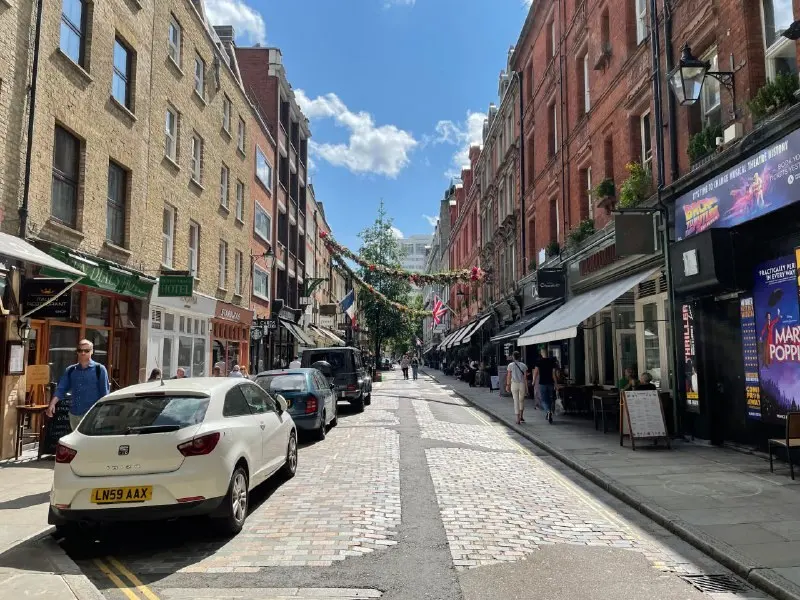 A narrow cobbled shopping street in London lined with shops, awnings and signage