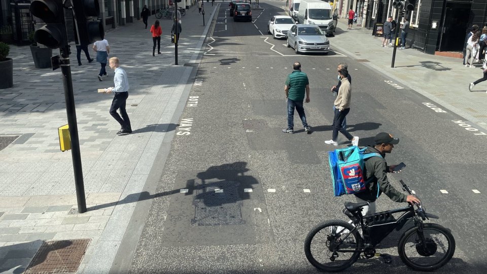 A delivery rider with a courier bag at a junction in the City of London