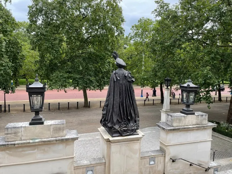 A monument against lawn and trees in a London park, with a path and lamp posts beyond