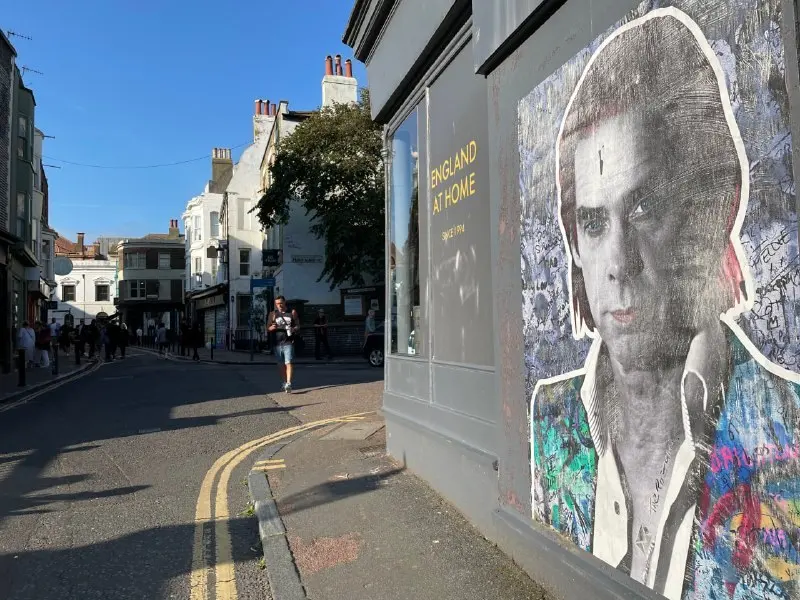 A British shopping street with shops at street level and a large painted portrait on a gable wall