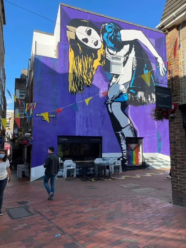 A large street-art mural on the end of a building, purple wall and bunting above the street
