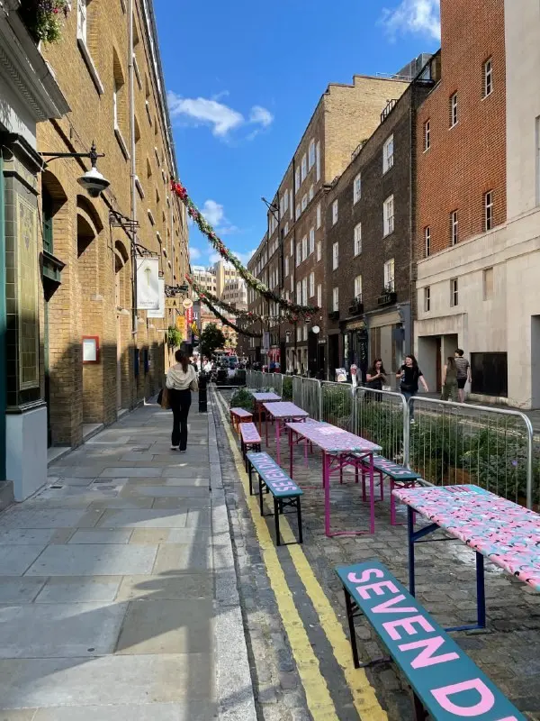 Narrow Soho street with brick buildings and pink benches along the pavement