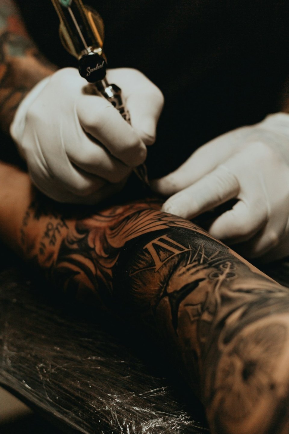 A gloved tattoo artist tattooing an arm