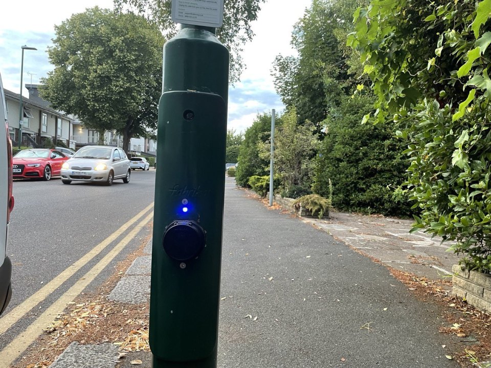An on-street electric-car charging post on the pavement of a residential British street, parked cars beyond