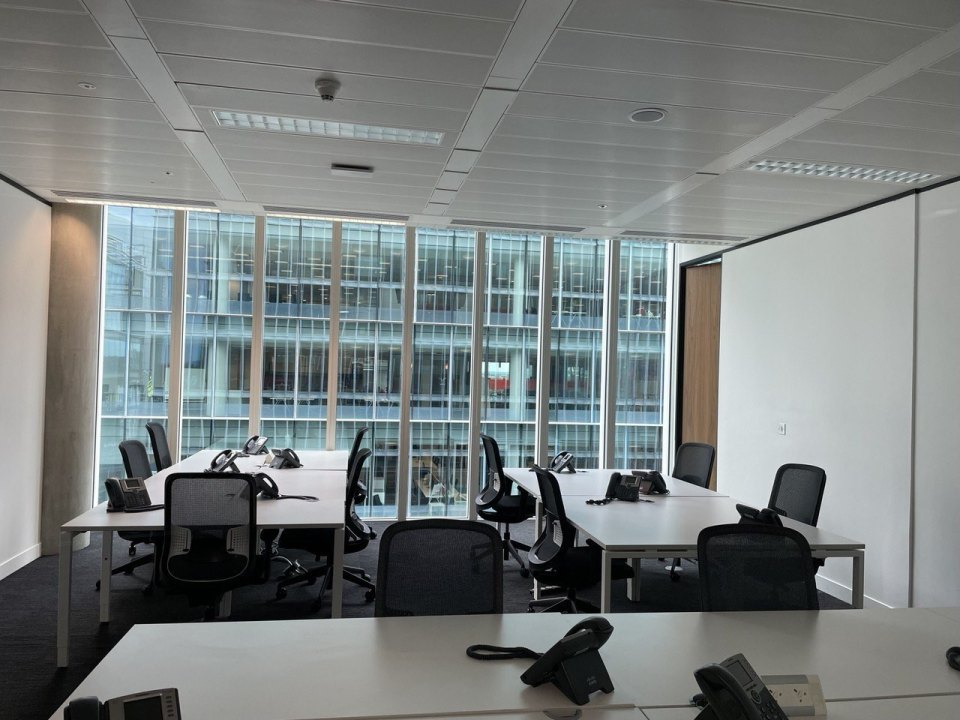 Empty desks in a British open-plan office with desk phones, a glass office block outside the window