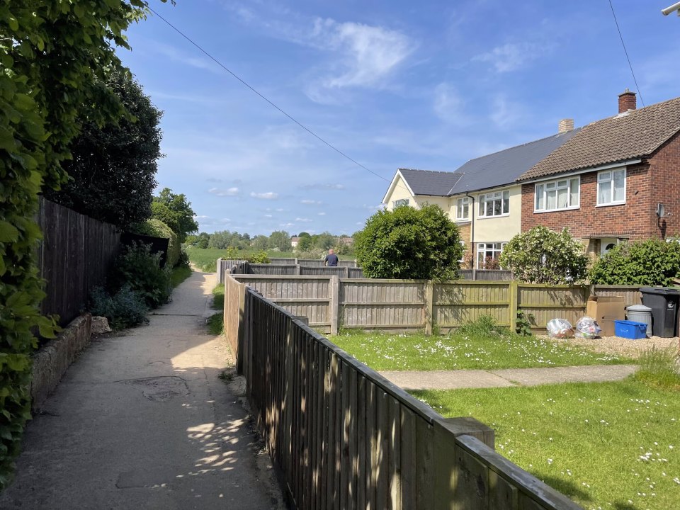 A path between the back gardens of English houses, wooden fences