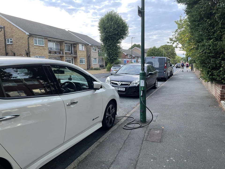 A residential street in a British suburb, an electric car charging from a lamppost