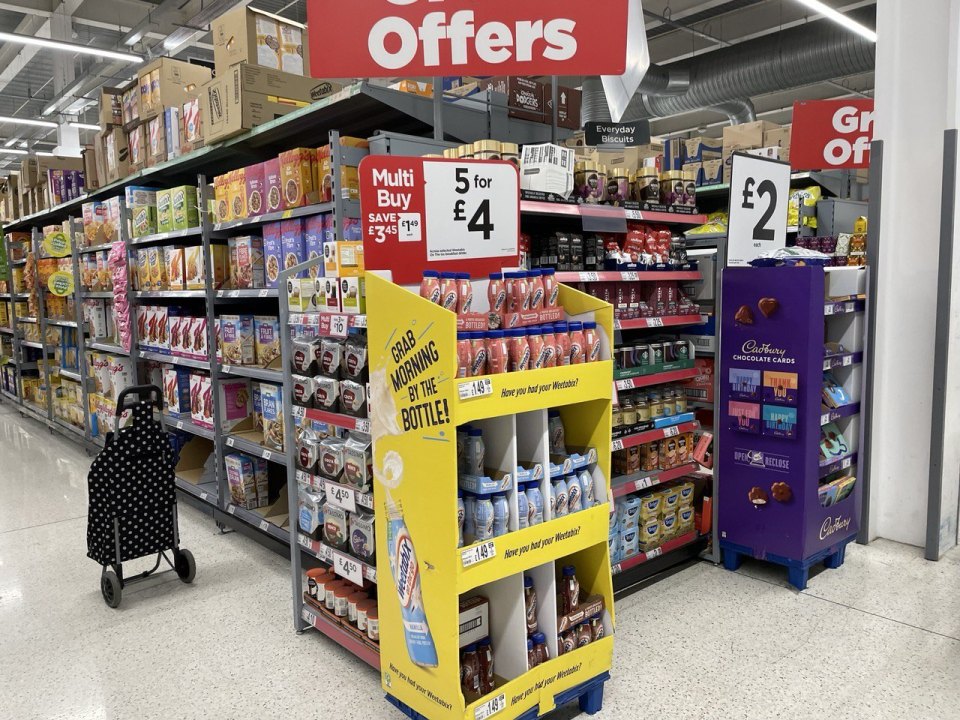 A British supermarket aisle with "5 for £4" offer signs and a wheeled shopping trolley