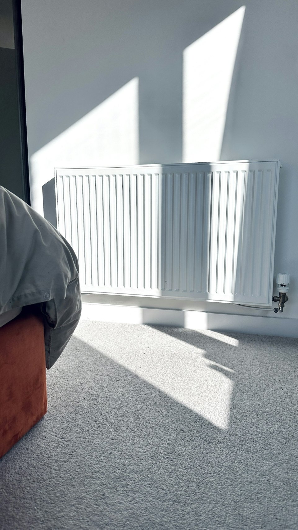 A white central-heating radiator under a window in a bright room