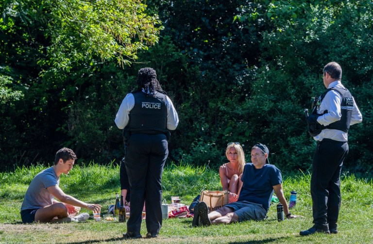 A police officer speaks to people relaxing by the Serpentine in Hyde Park, London 