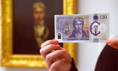 Человек держит полимерную банкноту в 20 фунтов стерлингов перед портретом художника JMW Turner в Тейт Британия в Лондоне.
